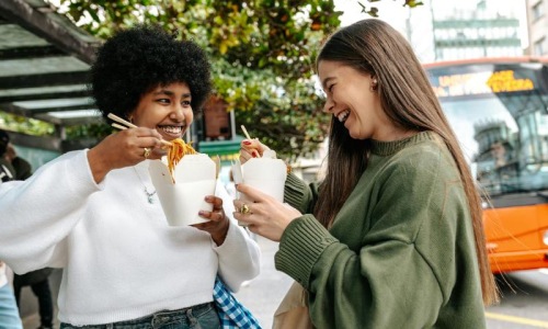 Two women laughing and eating street food in the city.
